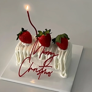 Red acrylic Merry Christmas cake topper on a white cream cake with fresh strawberries