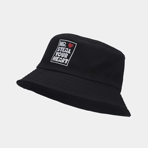 Détail d'un bob en toile noire avec écusson en forme de cœur et broderie blanche