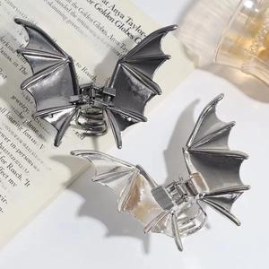 Detailed view of metal bat-shaped hair claws in silver and gun grey on an open newspaper