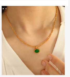 Dettaglio di un ciondolo ovale in pietra verde con catena dorata indossata da una modella