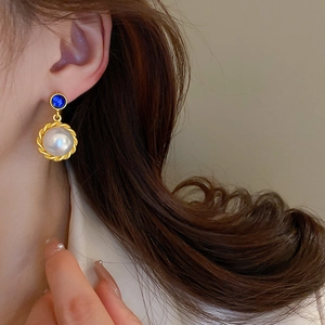 Detail of vintage gold-tone earrings with blue studs and white pearls on a female model