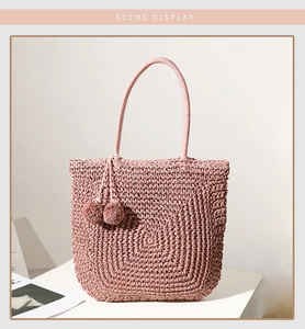 Detail of pink woven straw handbag featuring decorative pom-poms and textured handle