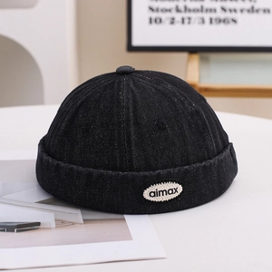 Close-up of black denim docker cap with stitched aimax logo tag and premium cotton texture