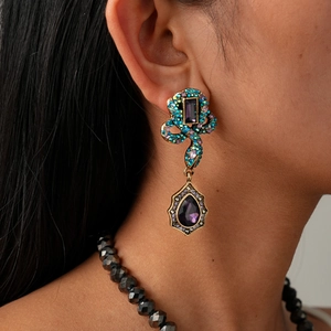 Detail of vintage snake drop earring with purple crystals and antique gold finish