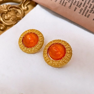 Macro shot of vintage round gold earrings with orange gemstone and hollow floral edges