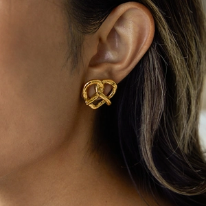 Close-up of a gold knot heart earring worn by a model to show texture and style