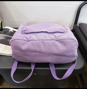 Detail of purple canvas backpack showing durable bottom structure and wide shoulder straps