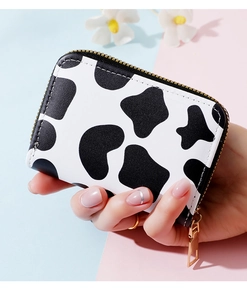 Detailed view of women's compact cow print card holder with gold zipper held by hand