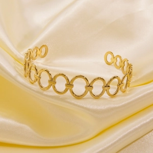 Detailed close-up of 14k gold plated stainless steel open bangle on cream silk fabric