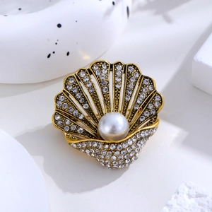 Detailed close-up of a golden shell brooch featuring sparkling rhinestones and a white pearl