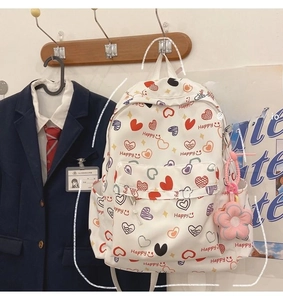 Detail of white backpack with heart prints and pink sunflower plush charm in campus setting