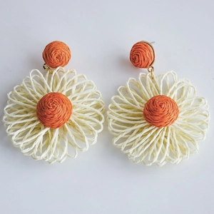 Detailed macro view of woven raffia flower drop earrings with orange centers and beige petals
