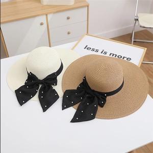 Detail of summer straw hats with black ribbon bows and pearl accents in khaki and beige