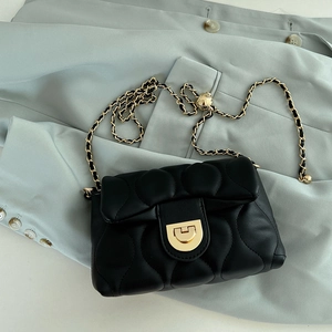 Black quilted chain crossbody bag with gold hardware placed on a light green suit jacket