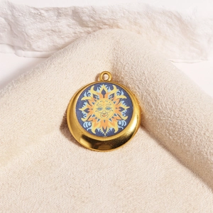 Detail shot of a golden sun face pendant with blue enamel on a soft beige towel texture