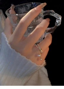 Detail of a gold-plated pearl ring with pavé crystals worn by a hand holding a glass