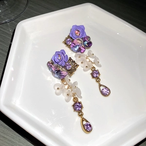 Detail view of purple crystal heart and floral resin earrings on a white porcelain plate