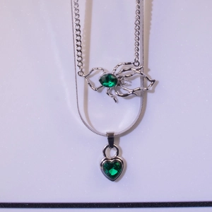 Double-layered silver necklace with emerald green heart pendant and spider design