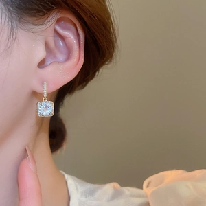 Close-up of elegant gold square zircon earrings on a model for a luxury aesthetic look