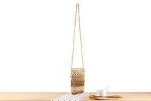 Detail shot of mini hand-woven gradient straw crossbody bag on a wooden table with coffee