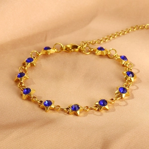 Macro detail of gold star bracelet with dark blue zircons on champagne silk background