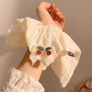 Detail of cream lace scrunchie with red cherry embroidery and bow on wrist