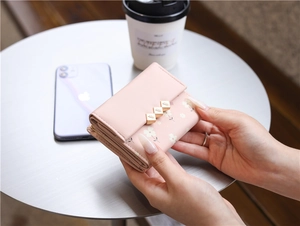 Detail view of pink floral tri-fold wallet held in hand over a minimalist desktop