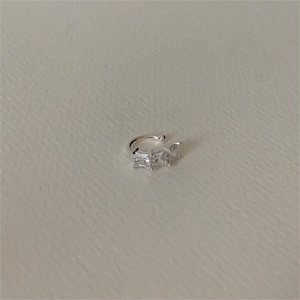 Detail of silver C-shape ear cuff with three square zircons on textured background