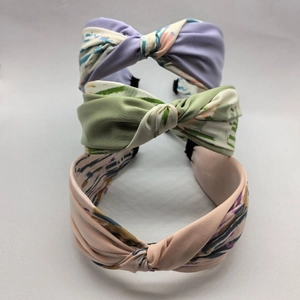 Three knotted fabric headbands in purple, green, and pink with abstract brush patterns