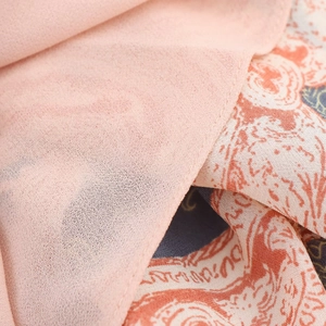 Détail du tissu en mousseline rose clair avec motifs floraux imprimés orange et bleu