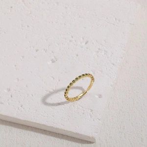 Detail of S925 stamped gold ring with green zircon stones on white stone base