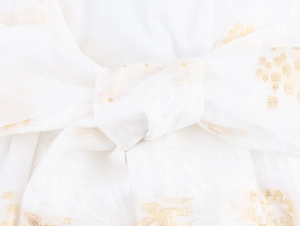 Dettaglio ravvicinato di un fiocco bianco con accenti floreali dorati sul vestito