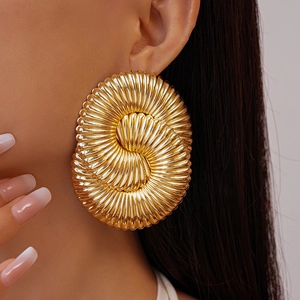 Gros plan de boucles d'oreilles dorées avec texture en spirale et fini miroir sur modèle
