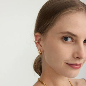 Dettaglio di orecchini a cerchio dorati e ear cuff con zirconi su una modella