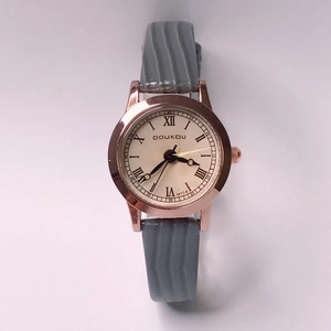 Detail of rose gold watch case with grey textured strap and Roman numeral dial