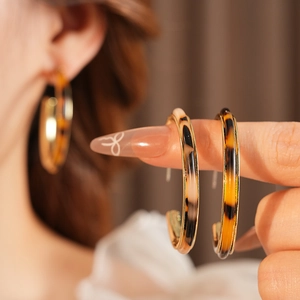 Close-up of tortoise shell resin C-shaped earrings with golden metal borders and 925 silver pins