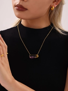 Détail d'un collier pendentif épingle doré avec pierres naturelles mauves sur pull noir