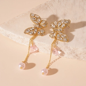 Close-up of golden butterfly fringe earrings with pink floral charms and pearls