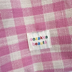 Close-up of pink checkered woven tote fabric with a white sozakka beauté brand label