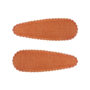 Détail de deux barrettes en tissu orange avec bords ondulés et texture de lin tissé