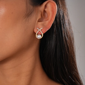 Close-up of elegant X-shaped gold earring with pearls and zircons worn by model