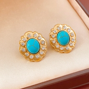 Vue macro de boucles d'oreilles fleur dorées avec turquoise et zircons sur soie