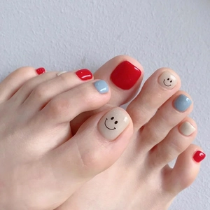 Close-up of red and blue press-on toenails featuring a minimalist black smiley face pattern