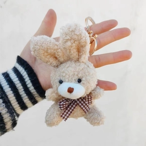 Détail d'un porte-clés lapin en peluche beige avec nœud à carreaux brun et fermoir doré