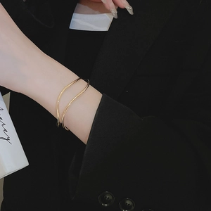 Close-up of golden double-layer wavy cuff bracelet worn on model wrist over dark suit