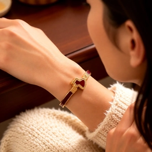 Detail of a gold-plated vintage bangle with a red wulu charm and intricate engravings