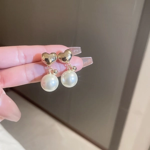 Detail view of heart-shaped gold stud earrings with elegant white pearl drops