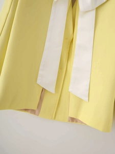 Detail of a bright yellow satin blazer featuring a large white decorative bow on the back