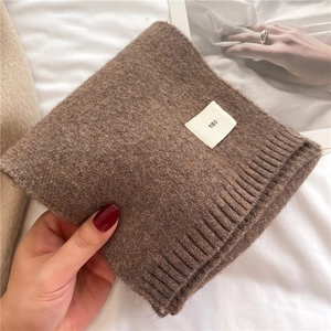 Detailed close-up of brown knit scarf fabric texture with a minimalist emo fabric label