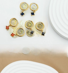 Detail shot of small gold hoop earrings featuring square blue, orange and black zircon stones